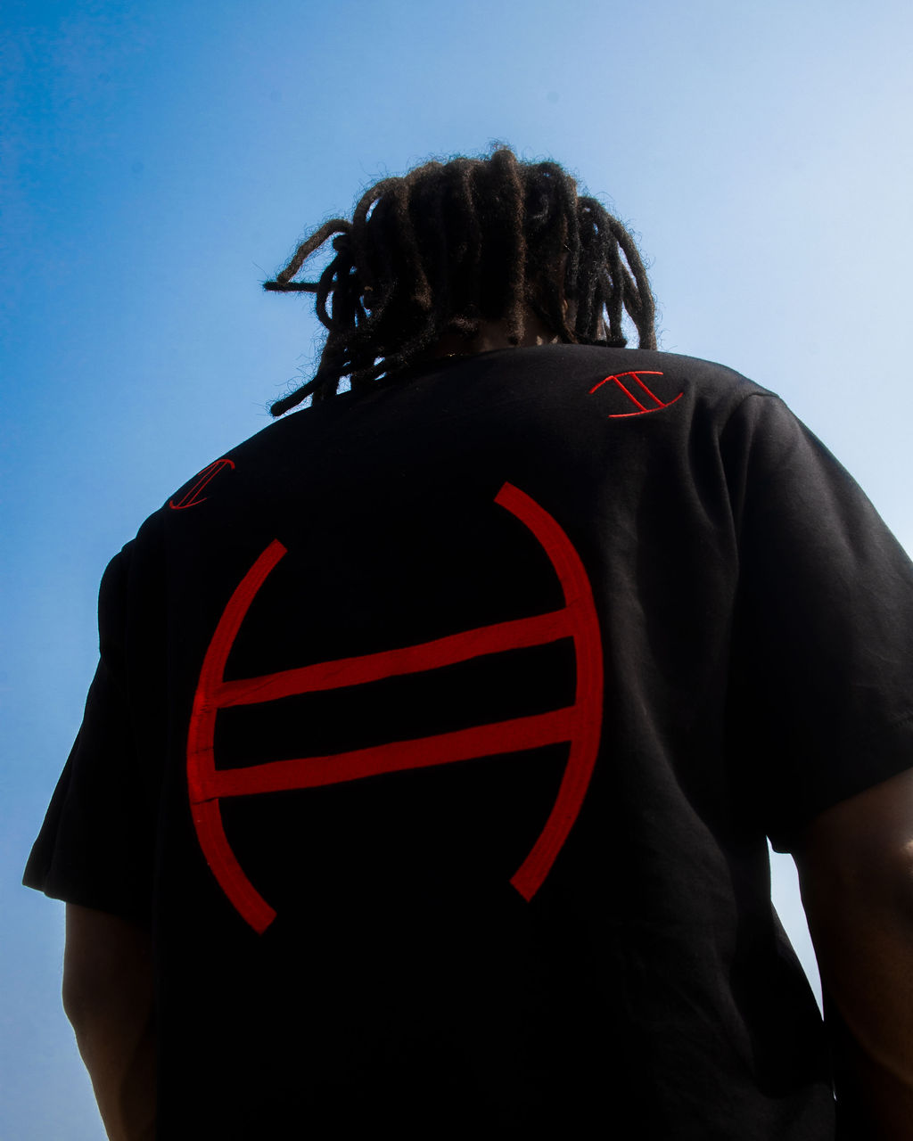 Person wearing a black t-shirt with red Nsibidi symbols against a blue sky