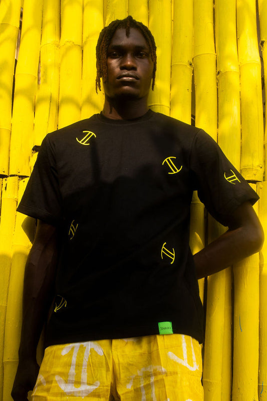 Person wearing a black t-shirt with yellow patterns and yellow shorts against a yellow background