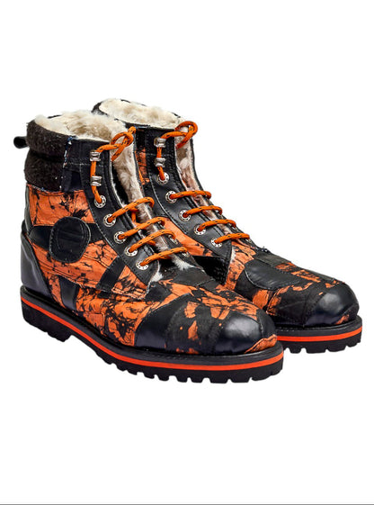 A pair of high-top lace-up boots featuring a black and orange splatter camouflage pattern, with a soft white shearling lining and orange laces, shown against a plain white background.