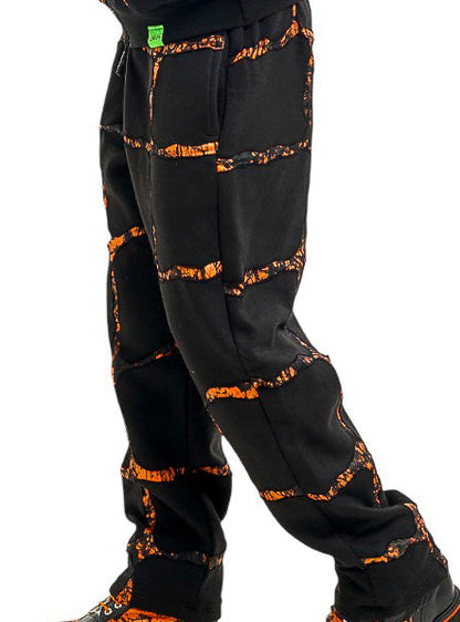 A man shown in profile wearing a matching black hoodie and jogger pants set with an orange abstract pattern, paired with black boots, against a solid white background.