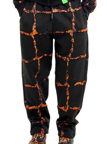 A man modeling a black zip-up hoodie and matching sweatpants set with an orange crackle or lava-like abstract pattern, photographed against a solid white background.
