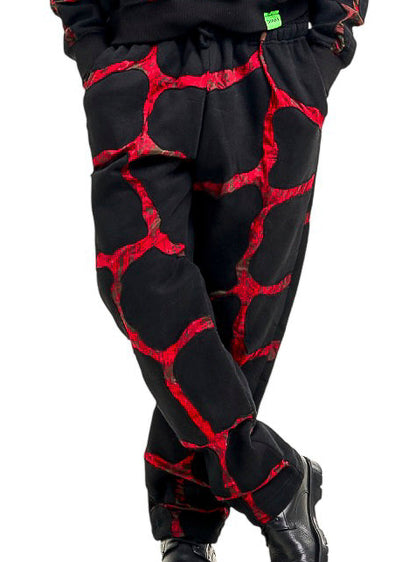 A man modeling a matching black and red patterned sweatpants set against a solid white background.