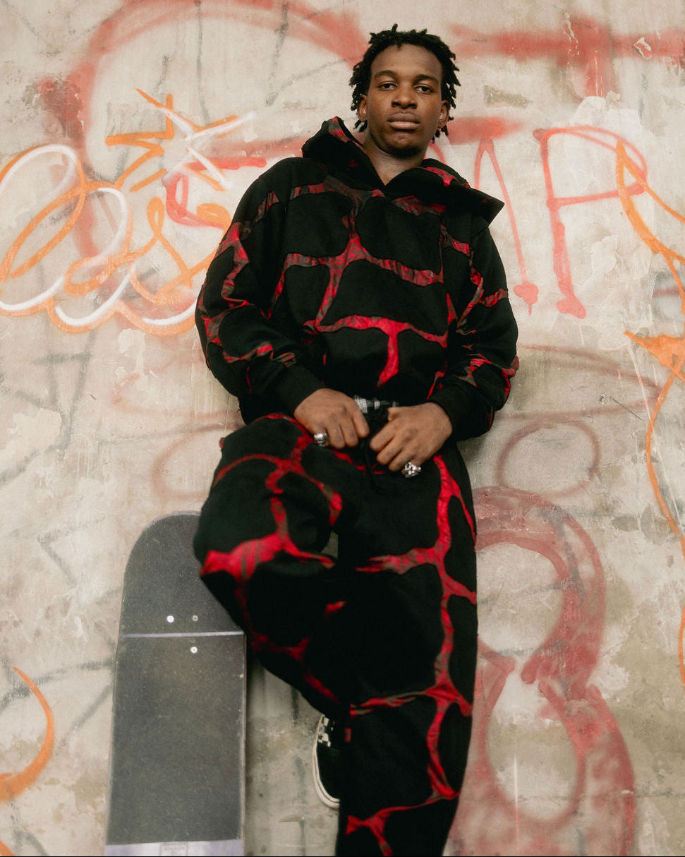 Person wearing a black and red outfit leaning against a graffiti-covered wall.