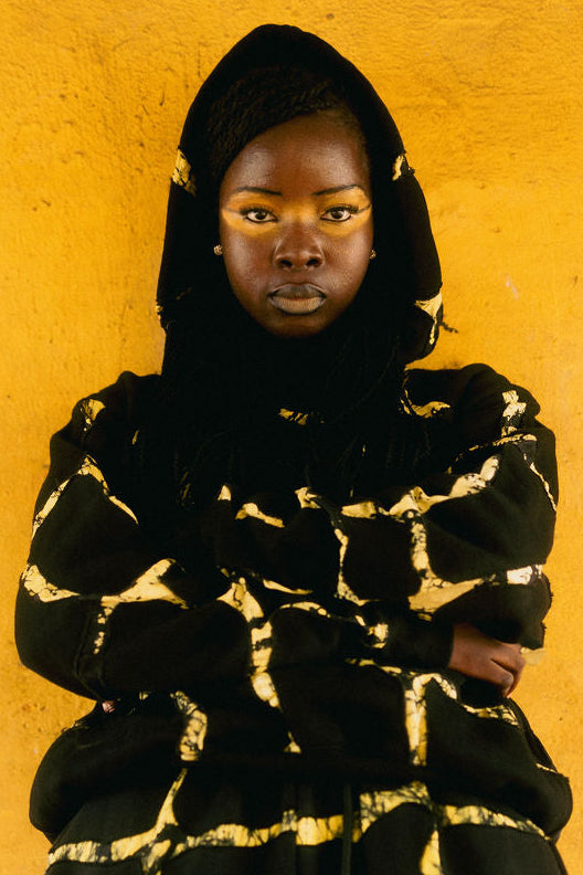 Person wearing a black and gold patterned outfit against a yellow background