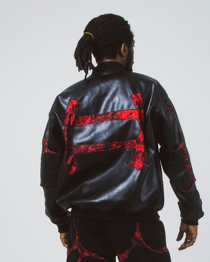 A model viewed from behind wearing a black leather bomber jacket and matching black pants with red nsibidi symbol on the back, set against a plain light gray studio background.