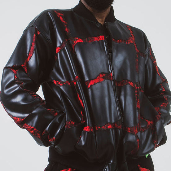 A man modeling a black shiny bomber jacket and matching black pants with a red cracked pattern, set against a plain light gray studio background.