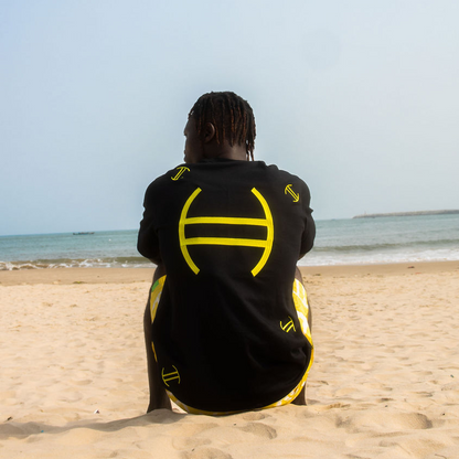 Person sitting on a beach wearing a black and yellow outfit with a logo.
