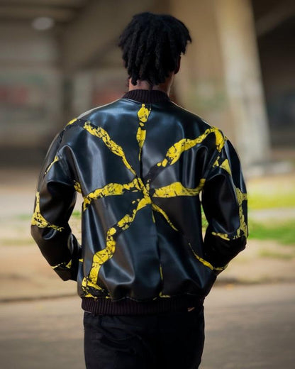 A person viewed from behind wearing a black leather bomber jacket with a bold yellow abstract paint splatter pattern across the back, set against a blurred outdoor background.